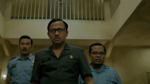 Penjaga penjara berjalan penuh kecurigaan di ruangan nomor 7 dalam film Miracle in Cell No. 7 sekuel