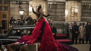 Cruella berdiri di atas mobil dengan gaya percaya diri