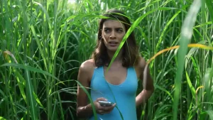 Becky DeMuth berjalan memasuki ladang rumput tinggi dalam film In the Tall Grass dengan ekspresi ragu dan suasana misterius